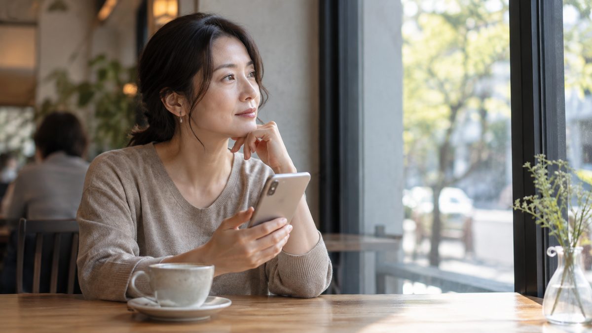 カフェでスマートフォンを見ながら考えごとをする人