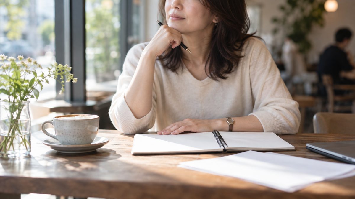 カフェのテーブルでノートを前に考えている40代の女性