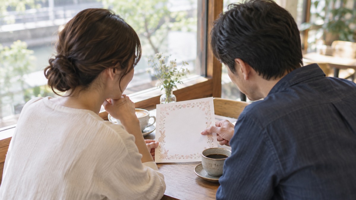 カフェで柄入りの用紙を見ながら話し合う日本人カップル