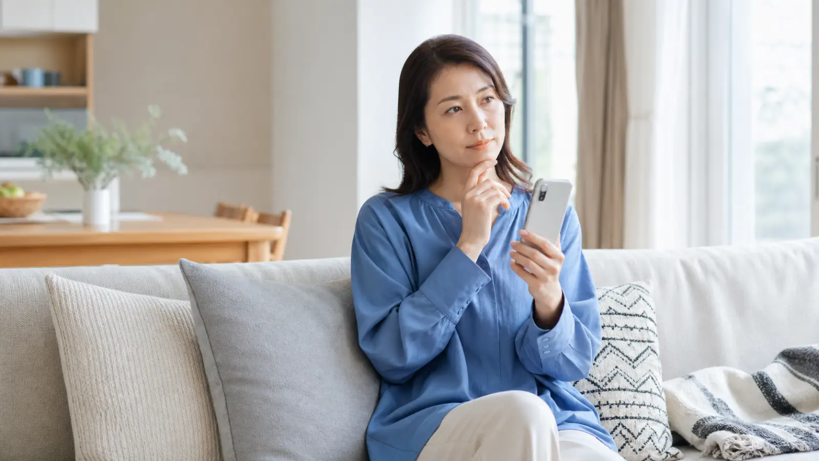 スマートフォンで情報を調べながら考え込む女性