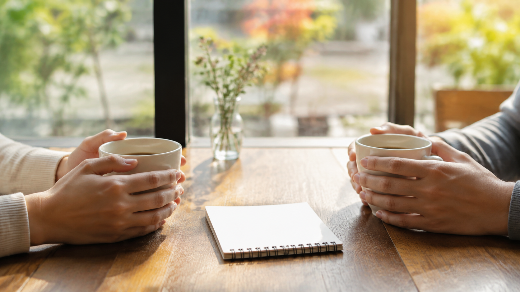カフェのテーブルで向かい合って話す2人分のコーヒーカップ